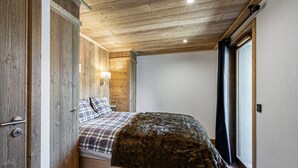 A wooden-paneled room with a bed, a nightstand, a wall-mounted lamp, and a window with curtains. - Lovely apartment in Courchevel Le Praz, close to slopes, with parking and wifi (Courchevel)