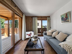 Ein gemütliches Wohnzimmer mit grauem Sofa, Holzboden, einem Couchtisch mit Flasche und Gläsern sowie einem Bild an der Wand.