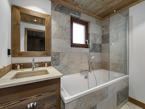 A bathroom with a wooden vanity, a large mirror, a bathtub, and a shower enclosure.