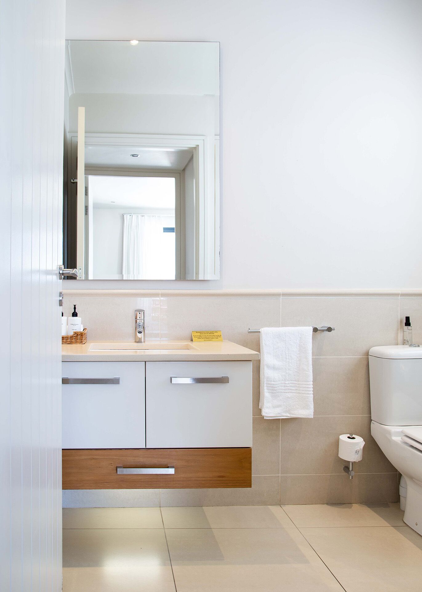 A modern bathroom with a white vanity, a mirror, a towel rack, and a toilet.