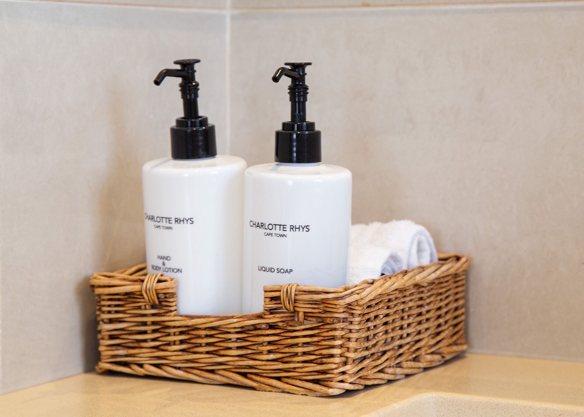 Two bottles of Charlotte Rhys products, one hand and body lotion and one liquid soap, in a wicker basket.