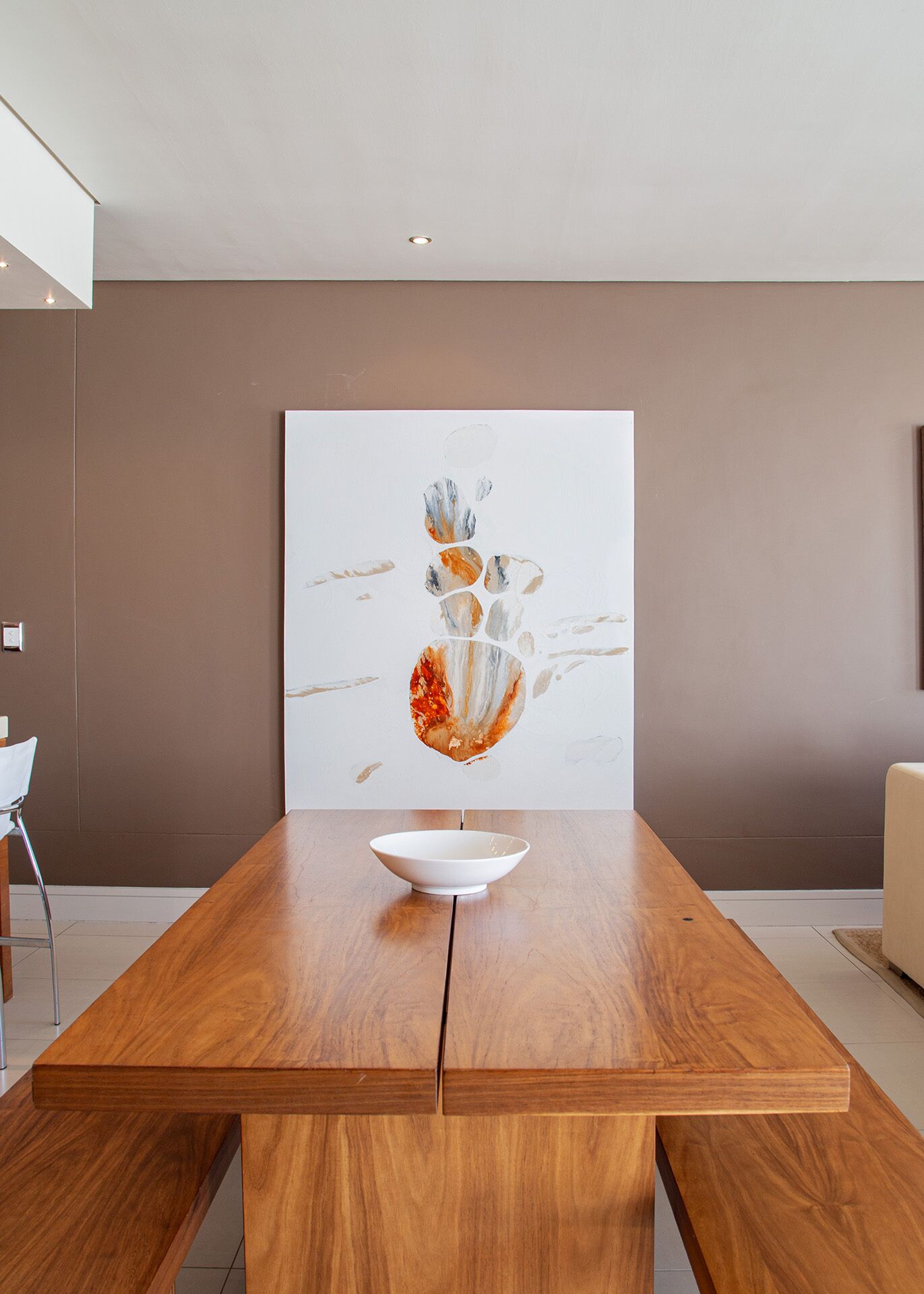 Un comedor moderno con una mesa de madera, un tazón blanco y un cuadro abstracto grande en la pared.