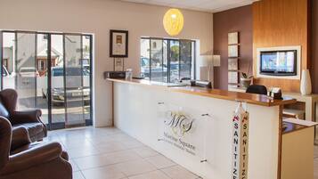 A hotel reception area with a reception desk, a chair, a television, and a sign indicating a sanitization station.