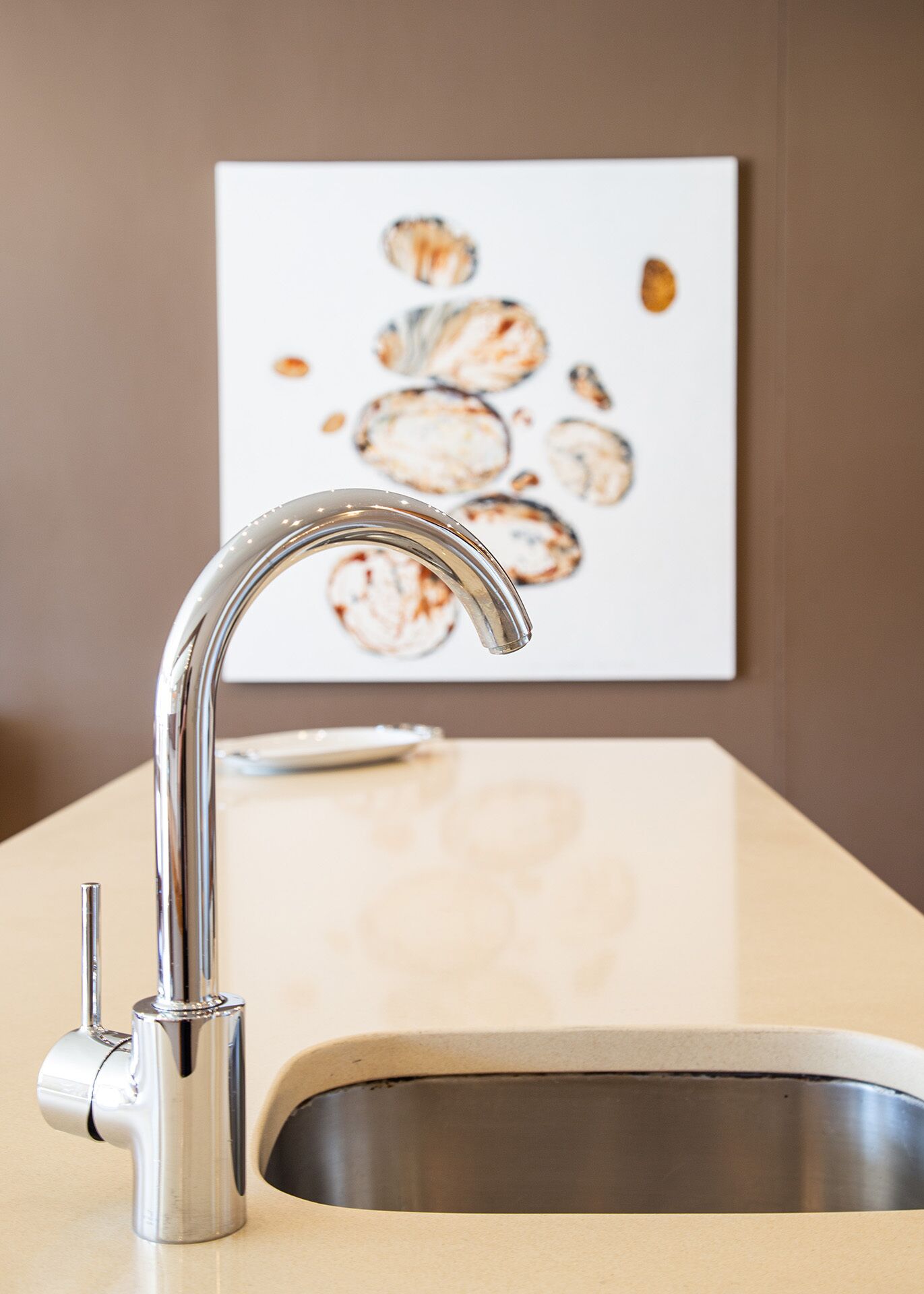 A modern kitchen with a stainless steel sink and faucet, a beige countertop, and a wall-mounted artwork.