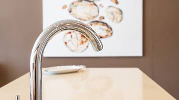 A modern kitchen with a stainless steel sink and faucet, a beige countertop, and a wall-mounted artwork.