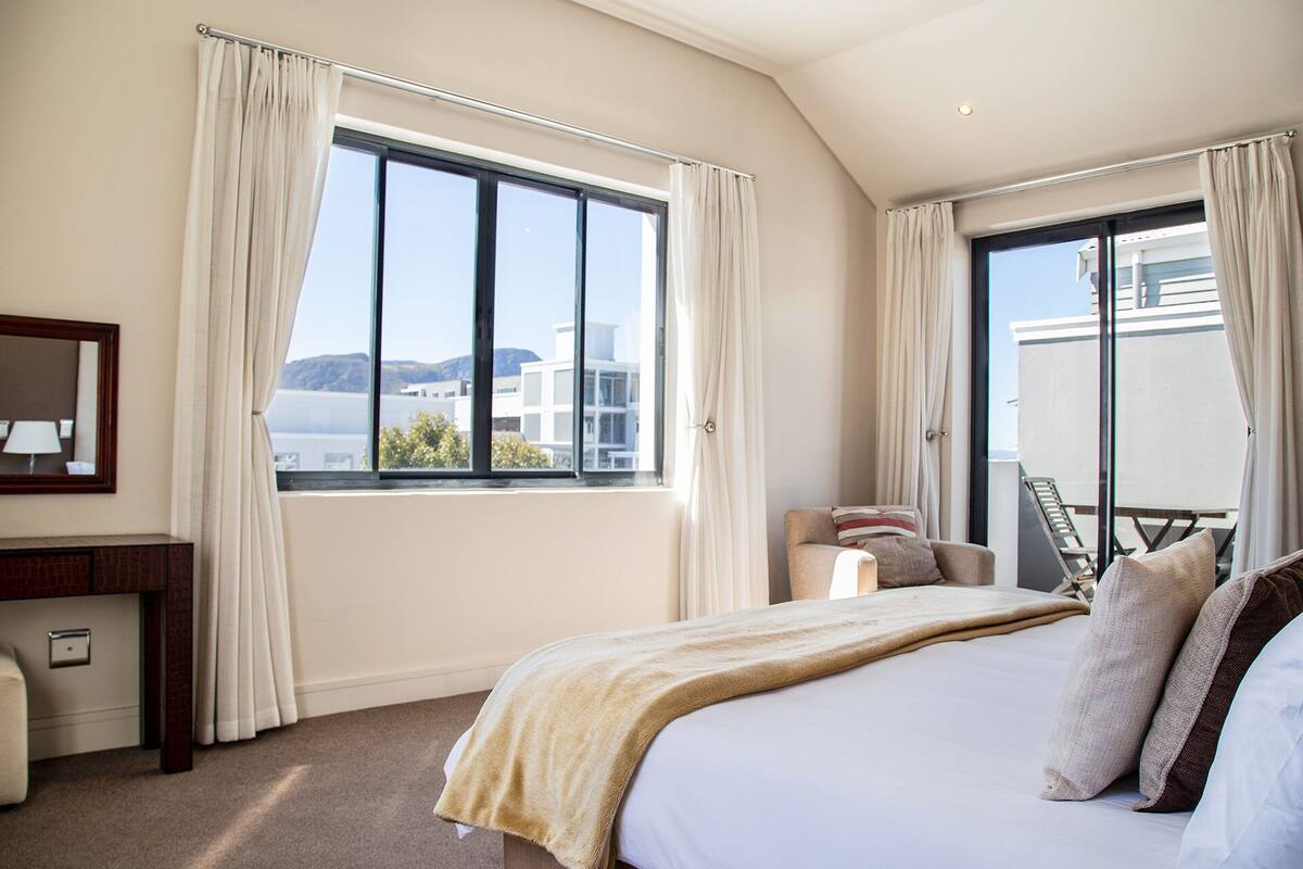 A hotel room with a large bed, a chair, a desk, and a view of the sea.