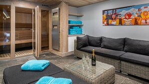 A spa room with wooden walls and ceiling, a gray sofa, a wicker coffee table, and a painting on the wall. - Luxury chalet with pool and spa in Courchevel (Courchevel)