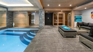 A modern indoor pool area with a stone floor, wooden ceiling, and a seating area with a sofa and cushions. - Luxury chalet with pool and spa in Courchevel (Courchevel)