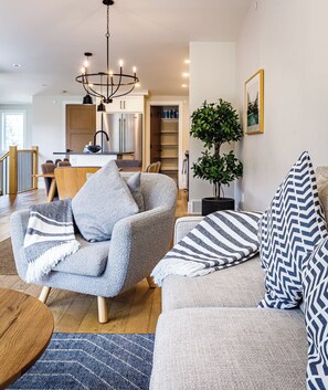 A modern living room with a grey armchair, a sofa with patterned cushions, a wooden coffee table, and a blue rug. - Rundleview - Impeccable Design and Private Hot Tub (Canmore)