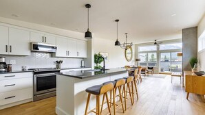 A modern kitchen with white cabinets, a central island with bar stools, and pendant lighting. - Rundleview - Impeccable Design and Private Hot Tub (Canmore)