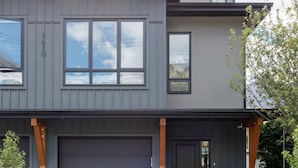 A modern two-story house with a dark grey exterior, a large garage door, and a driveway leading to the entrance. - Rundleview - Impeccable Design and Private Hot Tub (Canmore)