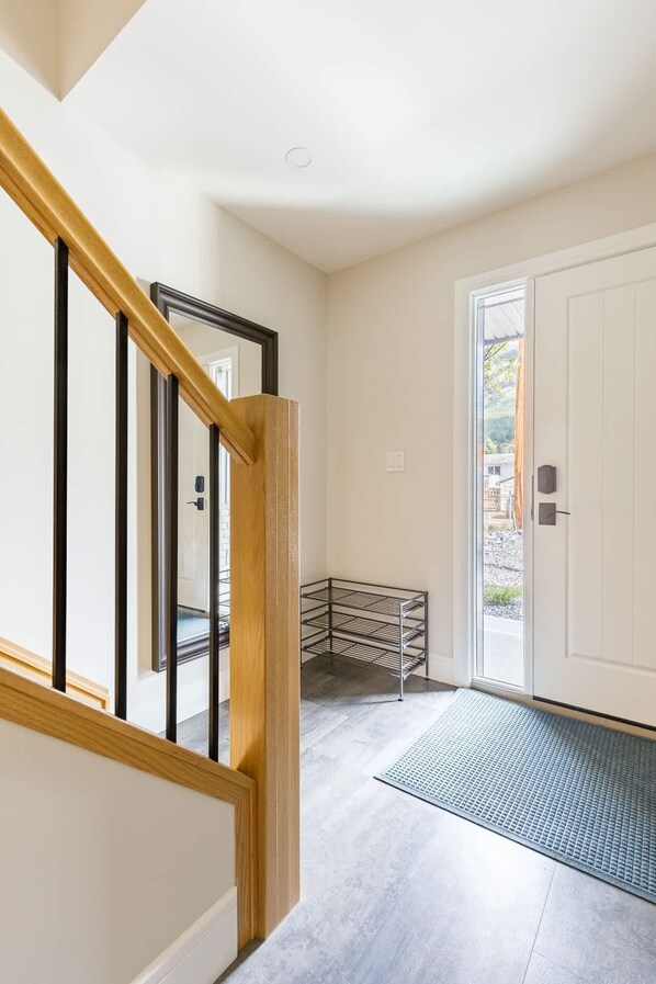 A clean, modern hallway with a wooden staircase, a glass door leading outside, and a metal rack against the wall. - Rundleview - Impeccable Design and Private Hot Tub (Canmore)
