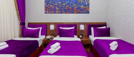 A hotel room with three beds, each with purple bedding and white pillows. There is a large abstract painting on the wall above the beds.