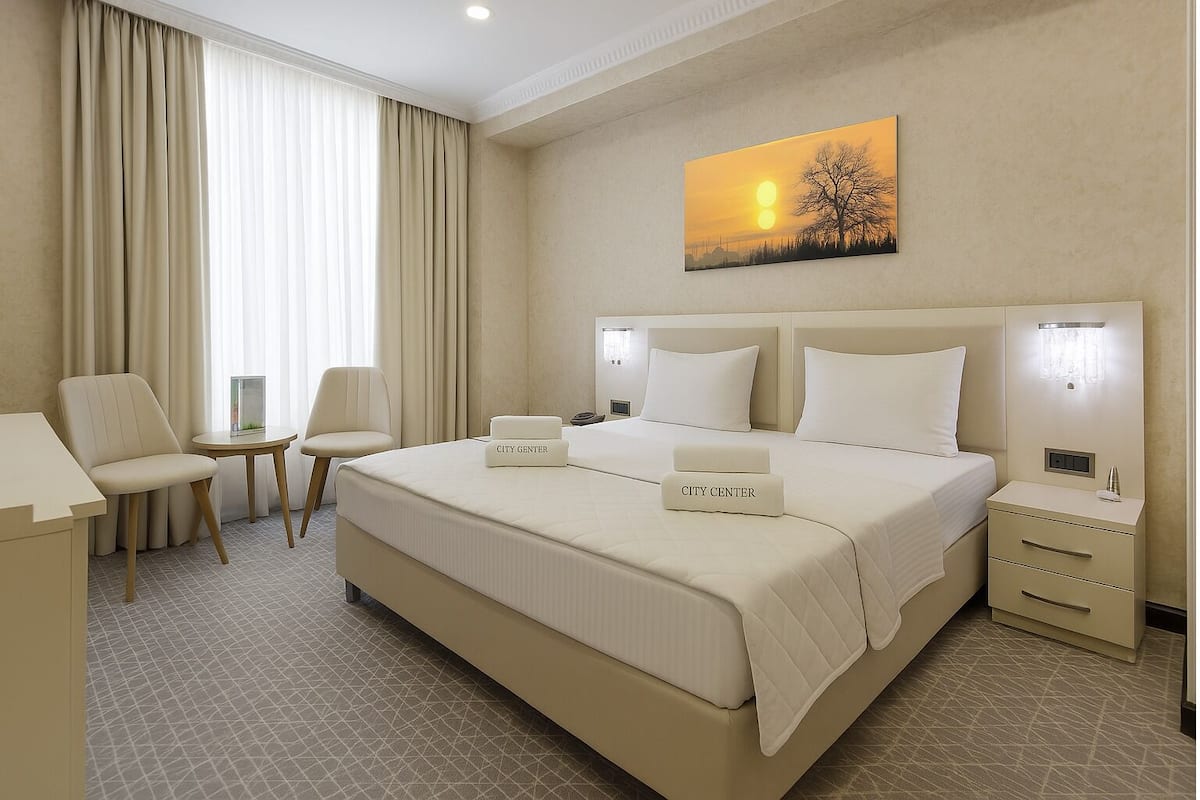 Ein Hotelzimmer mit einem großen Bett, zwei Nachttischen, einem Sessel, einem Schreibtisch und einem Bild an der Wand.
