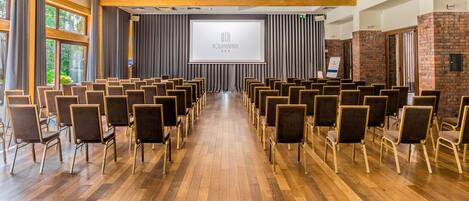 Un salón de conferencias con filas de sillas mirando hacia un escenario con una pantalla que muestra 'KOLUMAPARK'.