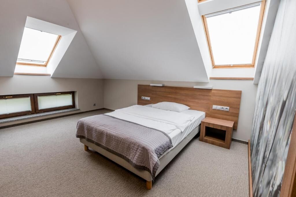 A bedroom with a sloped ceiling, skylights, a bed, bedside tables, and a small wooden stool.