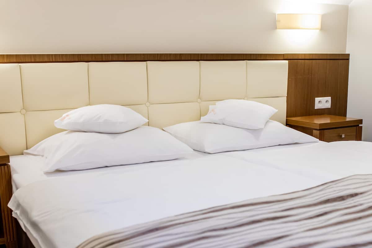 A hotel room with a large bed, two white pillows, a wooden headboard, a bedside table with a lamp, and a nightstand with a phone.