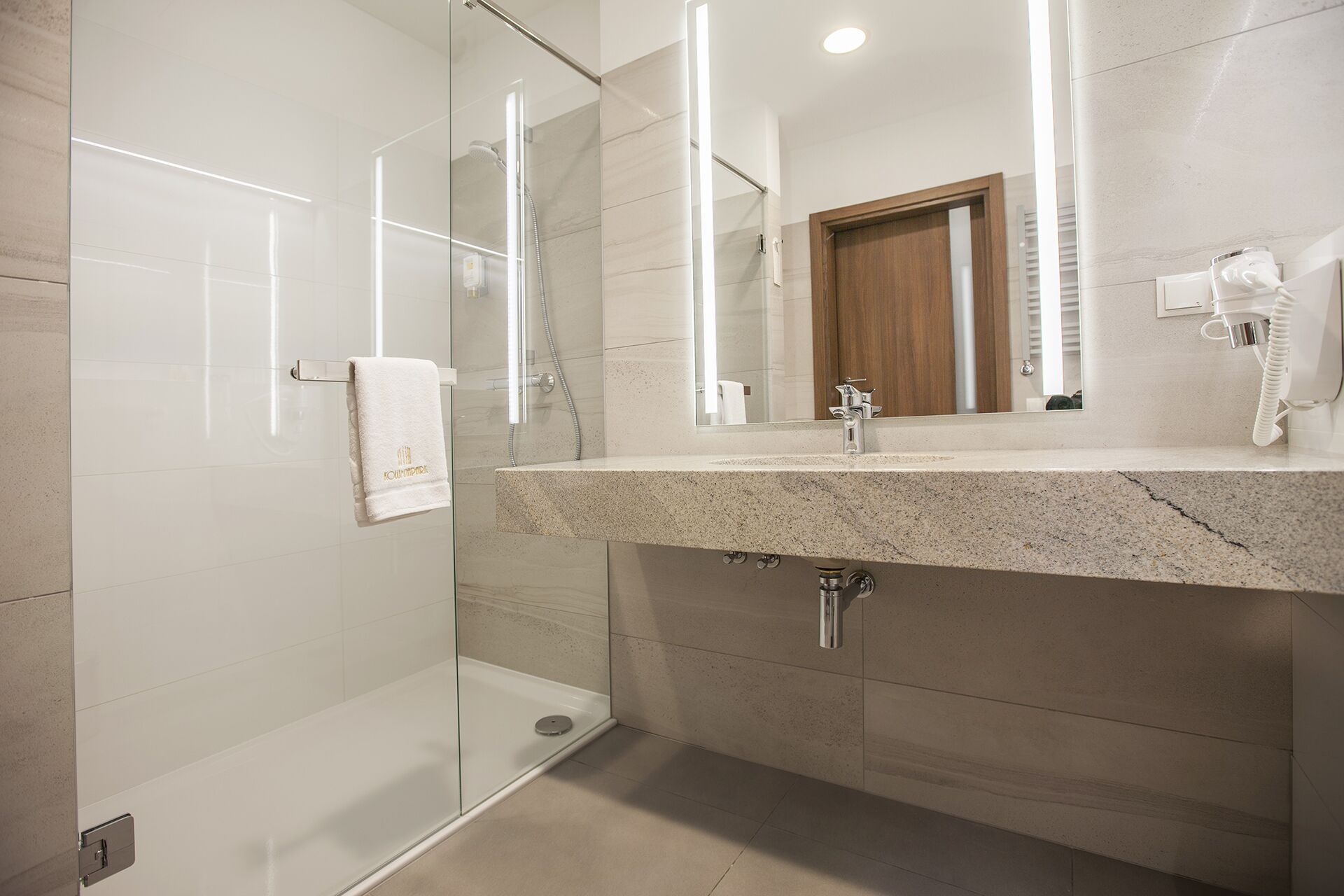 Un baño moderno con ducha de vidrio, encimera de granito y espejo sobre el lavabo.
