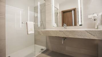 Un baño moderno con ducha de vidrio, encimera de granito y espejo sobre el lavabo.