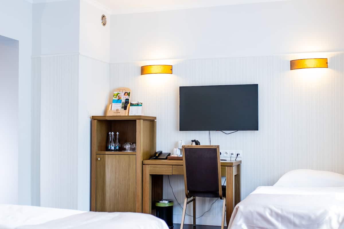 A hotel room with two beds, a desk with a chair, a television, and a minibar.