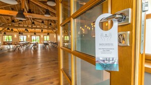 A conference room with wooden floors and tables, a wooden ceiling with hanging lights, and a door with a safety sign.