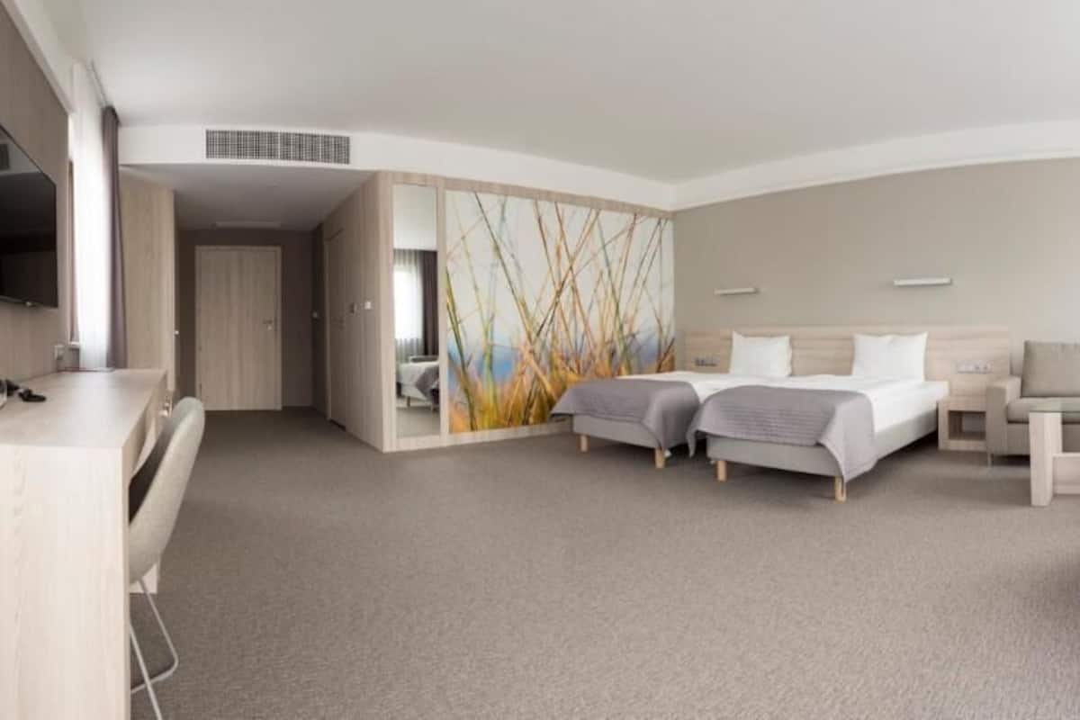 A modern hotel room with two single beds, a sofa, a desk, and a TV.