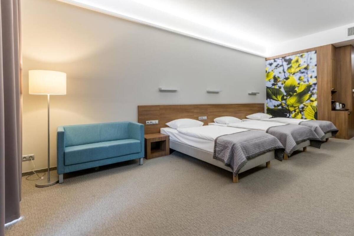 A hotel room with a bed, a blue sofa, a bedside table, and a wall-mounted lamp.