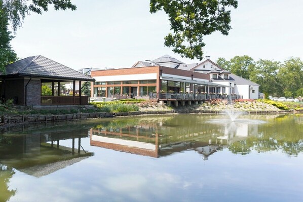 Hotel à beira do lago com um alpendre coberto, área de refeições com mesas ao ar livre e reflexo na água.