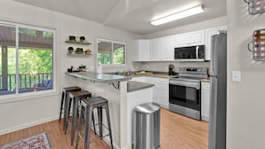 A modern kitchen with white cabinets, stainless steel appliances, and a bar area with stools.