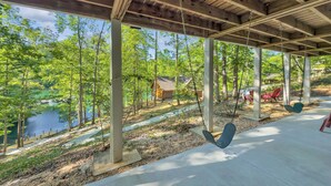 A covered outdoor area with swings, a concrete path, and a view of a lake and trees.