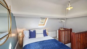A bedroom with a bed, a nightstand, a lamp, a wooden railing, and a skylight.