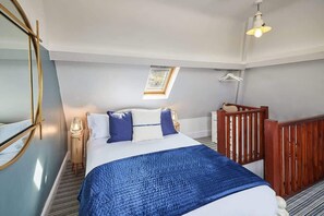A bedroom with a bed, a nightstand, a lamp, a wooden railing, and a skylight. - Host & Stay | No 3 Sandside (Whitby)