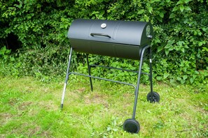 A portable barbecue grill on a grassy area with dense foliage in the background.