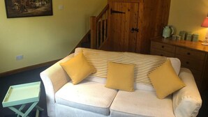 Um quarto aconchegante com um sofá branco, duas almofadas amarelas, uma mesinha lateral, uma escada de madeira e um quadro na parede.