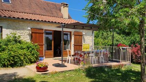 A stone house with a tiled roof, a covered patio with a table and chairs, and a garden with potted plants. - Quiet vacation rental for 5 people with a safe swimming pool (Salviac)