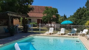 A swimming pool with a slide, surrounded by white lounge chairs and a covered area with a blue umbrella. - Quiet vacation rental for 5 people with a safe swimming pool (Salviac)