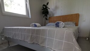 Ein Einzelbett mit grau-weißer Karodecke, einem Holz-Kopfteil und einem Blumentopf neben dem Fenster.