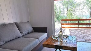 Ein moderner Wohnbereich mit grauem Sofa, einem Holztisch mit Dekoration und Blick auf eine Holzterrasse und Grünflächen.