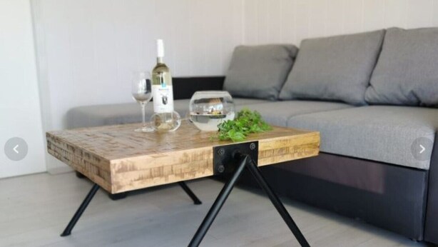 Ein Couchtisch aus Holz mit einer Weinflasche und Gläsern vor einer grauen Couch.