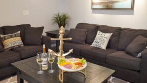 Ein Wohnzimmer mit einem dunkelbraunen Sofa, einem kleinen runden Tisch mit einer weißen Platte mit Snacks und zwei Weingläsern sowie einem Holzdekorstück.