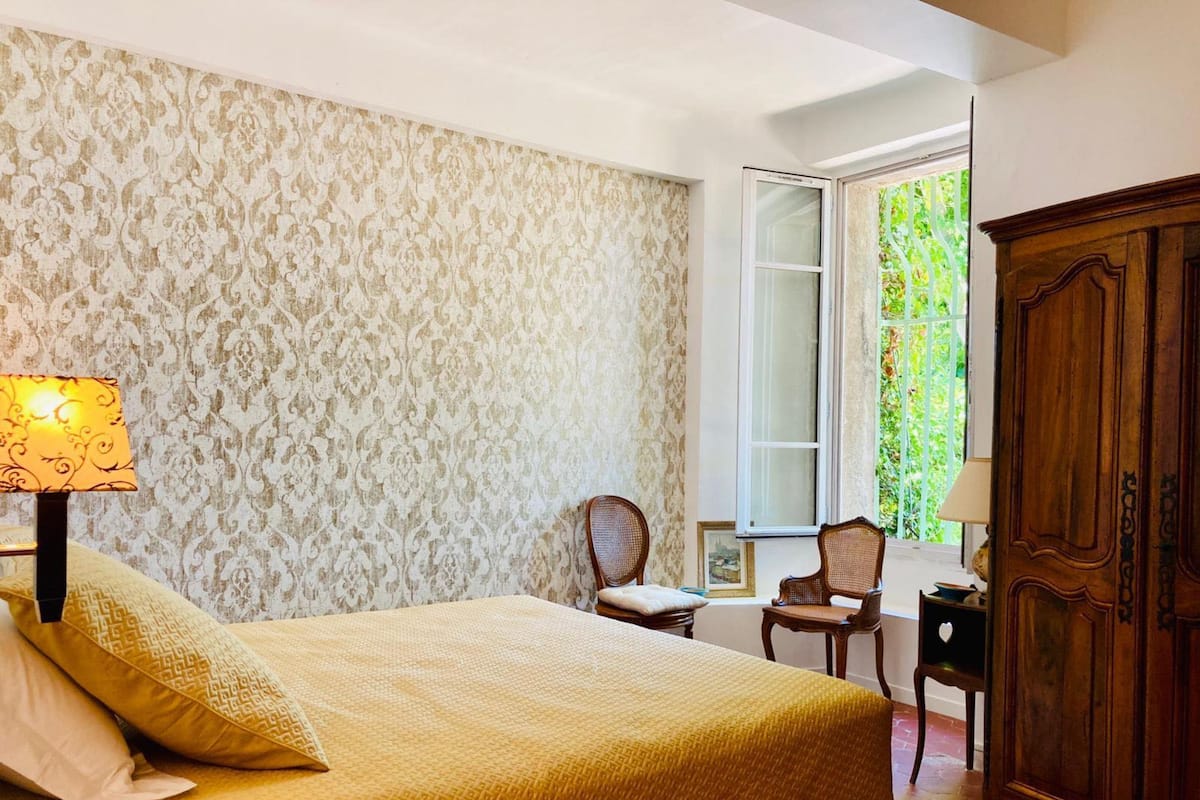 Un dormitorio con cama, mesita de noche, lámpara, silla y armario.
