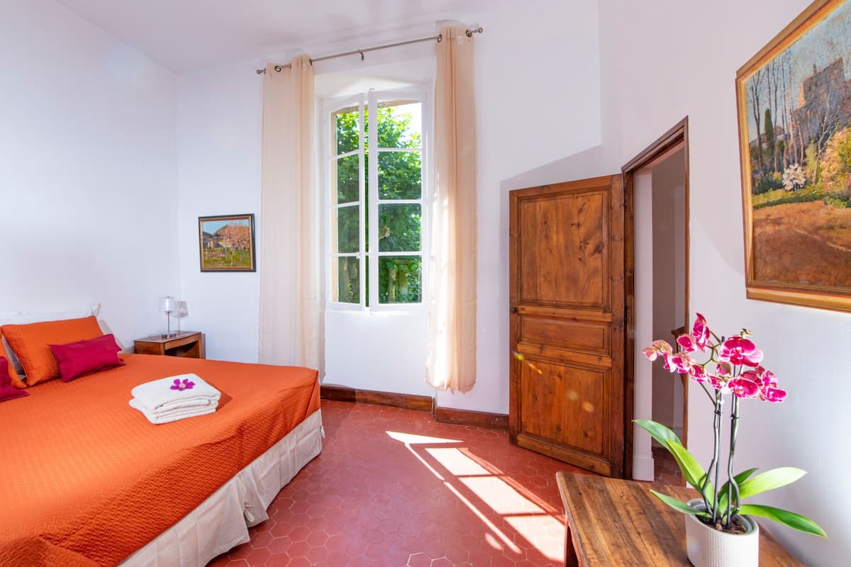Un dormitorio con una cama grande, un armario de madera, una ventana con cortinas y una orquídea en maceta.