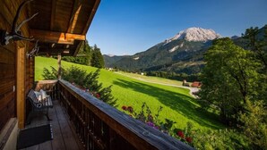 Un balcón de madera con un banco, con vistas a un campo verde y una montaña.