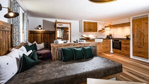 Ein gemütliches Wohnzimmer mit einer Couch, Holzelementen und einer Küche im Hintergrund.