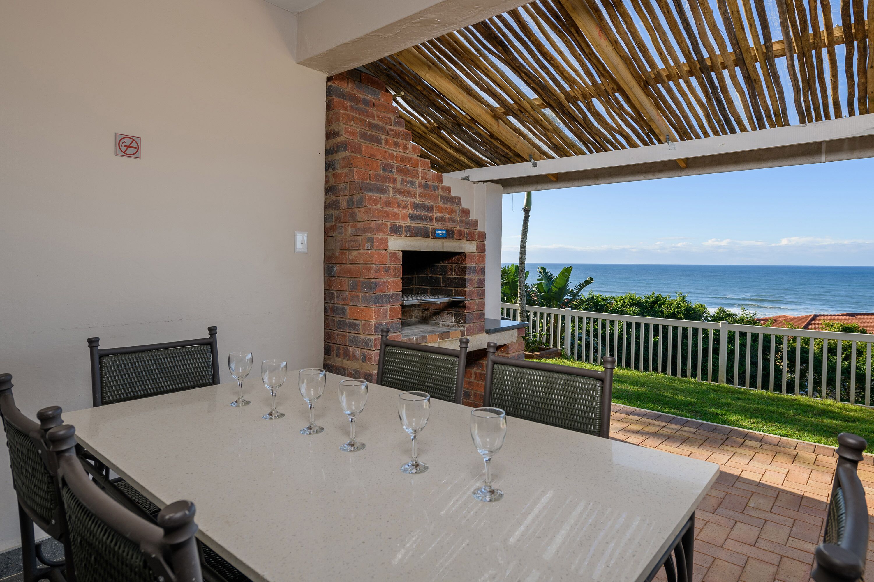 Un patio con chimenea de ladrillo, una mesa con copas de vino y vista al océano.