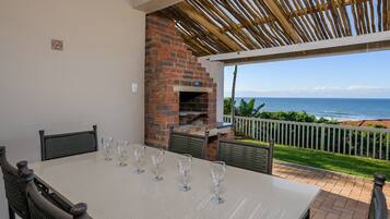 Un patio con chimenea de ladrillo, una mesa con copas de vino y vista al océano.
