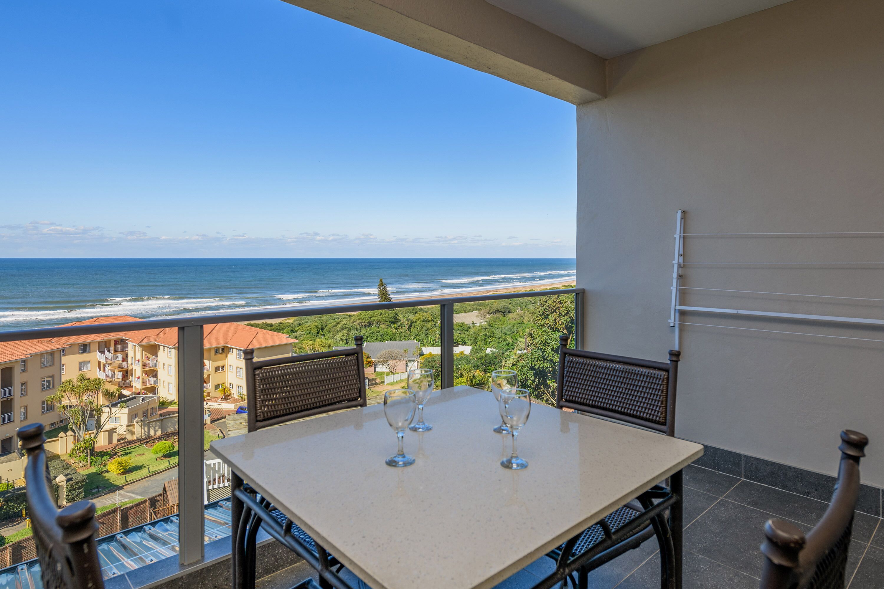 Un balcon avec une table et des chaises, donnant sur une plage et l’océan.