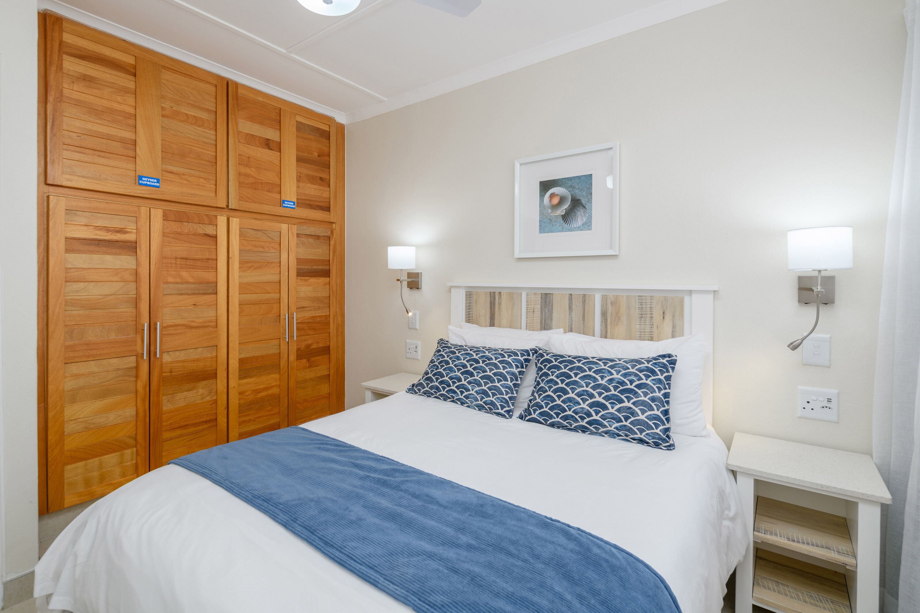 Quarto com cama, guarda-roupa de madeira, mesas de cabeceira e um quadro na parede.