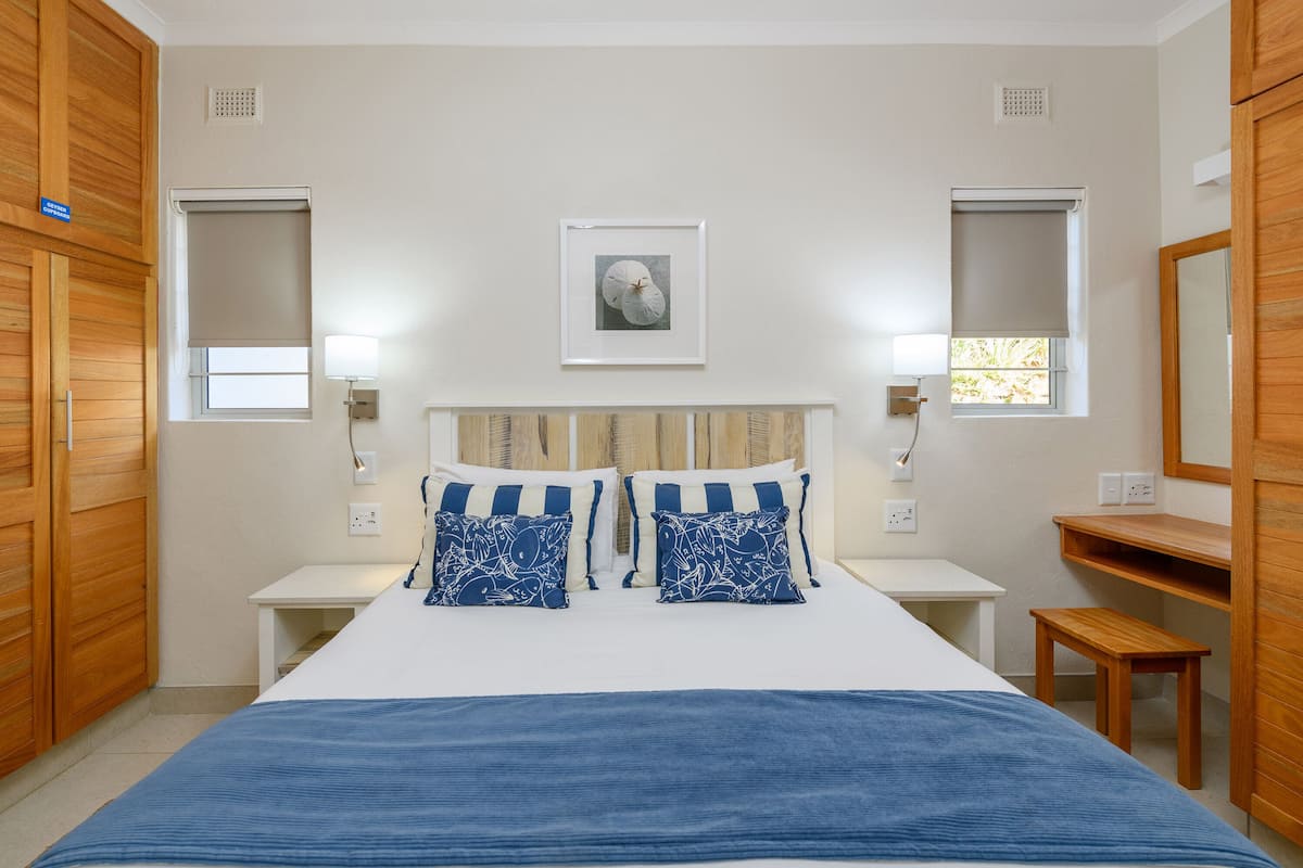 A bedroom with a large bed, two bedside tables, a wooden bench, and a mirror.