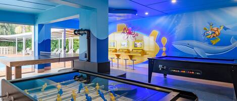 A room with a foosball table, a pool table, and a mural of a cartoon character.
